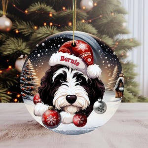 Personalize your holiday decor with this charming Bernedoodle Christmas ornament! Featuring a cute Bernedoodle in a festive Santa hat and customizable name, this round ornament adds warmth and joy to any tree. Perfect for dog lovers and unique gifts!