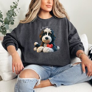 A woman wearing a Bernedoodle sweatshirt with cute design on the front and the back.  The front features a bernedoodle dog in claymation design holding a heart with his name, across the top of his head the words, "Doodle Mom".