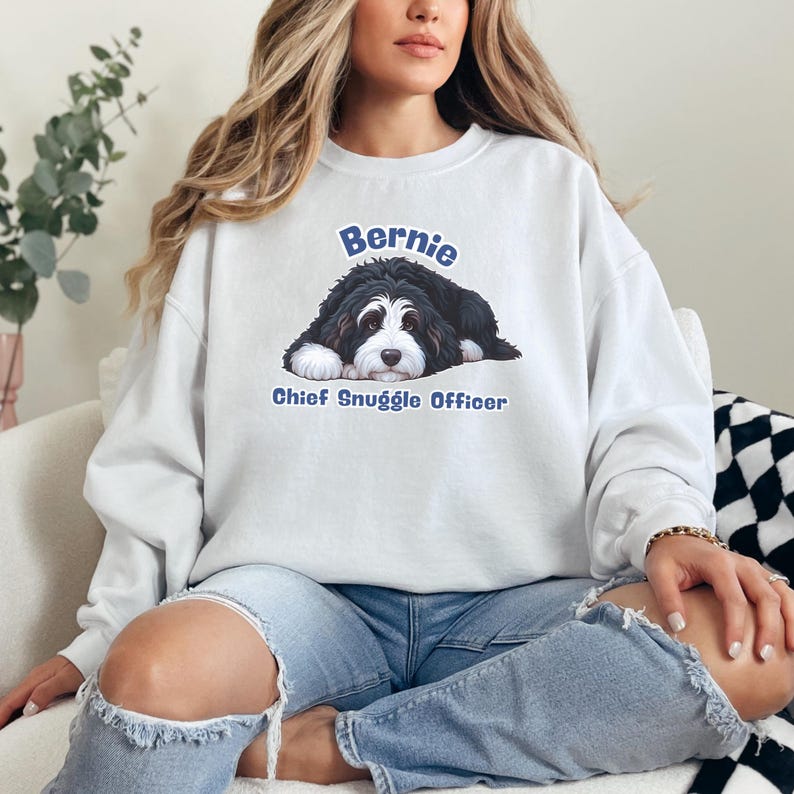 Puede incluir: Sudadera blanca con un gr&aacute;fico de un perro de monta&ntilde;a bern&eacute;s, el nombre "Bernie" arriba y "Chief Snuggle Officer" abajo. El perro es negro, blanco y marr&oacute;n. La sudadera es de estilo casual.