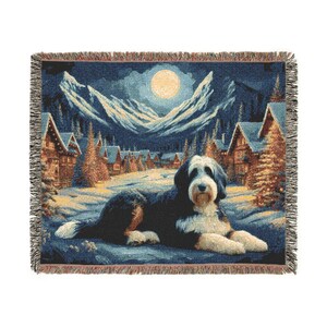 May include: Woven throw blanket featuring a black and white dog in a winter scene. The design includes snow-covered mountains, a full moon, and illuminated cabins. The blanket has a fringed edge and is primarily blue, white, and brown.
