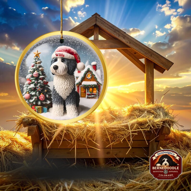 May include: A circular Christmas ornament with a Bernedoodle dog wearing a Santa hat, the name "Willis" is visible. The ornament has a gold border and shows a snowy scene with a Christmas tree and a house. The background includes a wooden structure and hay.