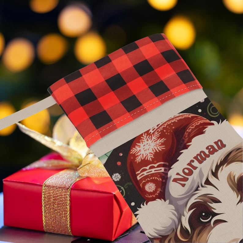 A festive Christmas stocking featuring a whimsical illustrated doodle dog wearing a red Santa hat, surrounded by holiday ornaments and greenery in a warm, detailed Christmas art style. The top of the stocking has a classic red and black buffalo-plaid cuff, and the stocking hangs from a white mantel decorated with evergreen garland and gold ornaments. The stocking design is personalized with your dog’s name, making it a charming and custom holiday décor piece for dog lovers.