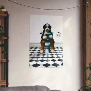 May include: A wall art print featuring a Bernese Mountain Dog sitting on a white toilet, holding a tablet. The dog has black, white, and brown fur. The floor is covered in a black and white hexagonal tile pattern, and a toilet paper holder is visible.