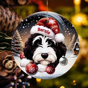 Personalize your holiday decor with this charming Bernedoodle Christmas ornament! Featuring a cute Bernedoodle in a festive Santa hat and customizable name, this round ornament adds warmth and joy to any tree. Perfect for dog lovers and unique gifts!