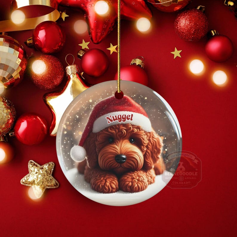 This ceramic ornament features a cute red mini-doodle golden doodle or goldendoodle dog wearing a Santa hat in a snow globe setting, surrounded by holiday decorations. Perfect for adding a festive touch to your Christmas tree or as a thoughtful gift for dog lovers.