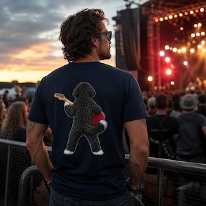 May include: A dark navy blue short-sleeved t-shirt featuring a graphic on the back of a fluffy black dog with white paws standing on its hind legs while holding a light-colored electric guitar and a red heart-shaped object against its side.