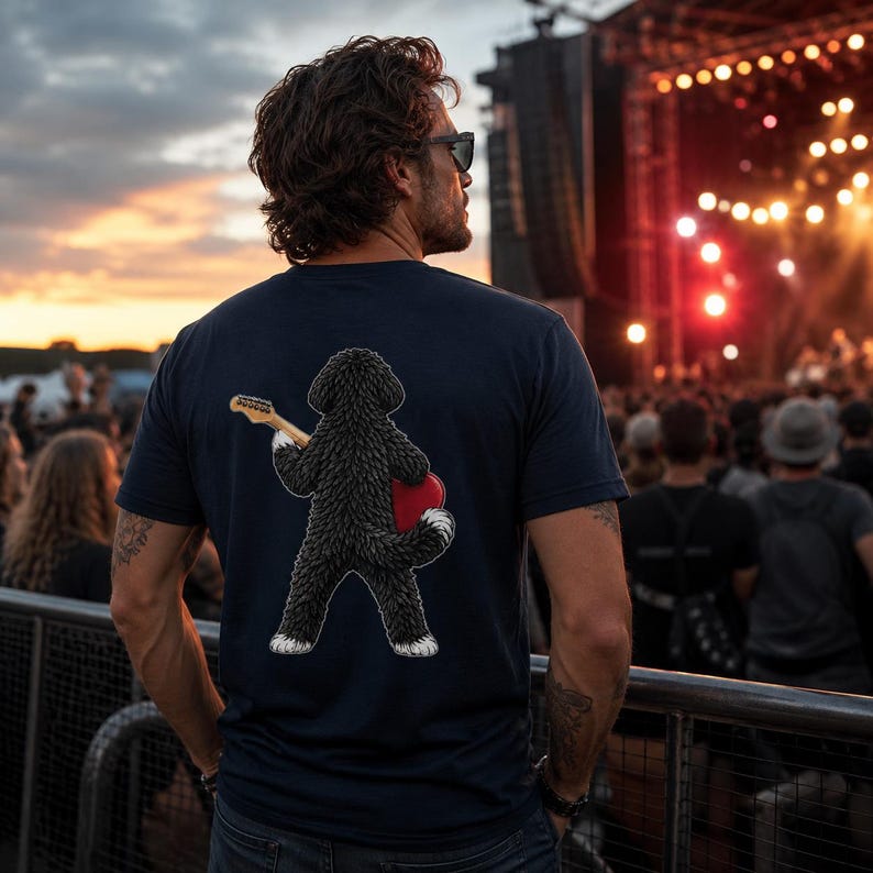 May include: A dark navy blue short-sleeved t-shirt featuring a graphic on the back of a fluffy black dog with white paws standing on its hind legs while holding a light-colored electric guitar and a red heart-shaped object against its side.
