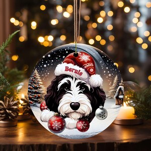 Personalize your holiday decor with this charming Bernedoodle Christmas ornament! Featuring a cute Bernedoodle in a festive Santa hat and customizable name, this round ornament adds warmth and joy to any tree. Perfect for dog lovers and unique gifts!