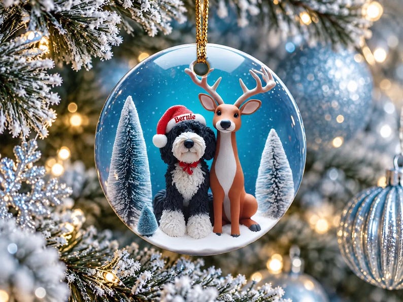 May include: A round ceramic Christmas ornament featuring a black and white dog wearing a red Santa hat with the name Bernie printed on it, sitting next to a brown deer in a snowy forest setting with pine trees under a blue sky.
