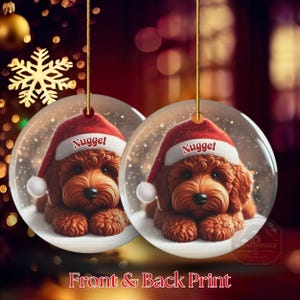 This ceramic ornament features a cute red mini-doodle golden doodle or goldendoodle dog wearing a Santa hat in a snow globe setting, surrounded by holiday decorations. Perfect for adding a festive touch to your Christmas tree or as a thoughtful gift for dog lovers.