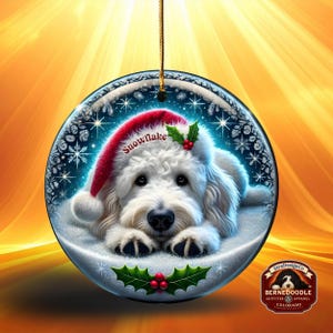 May include: A round Christmas ornament featuring a white dog wearing a red Santa hat with the word "Snowflake". The dog is lying in snow, surrounded by snowflakes. Holly and berries decorate the bottom. A gold string is attached for hanging.