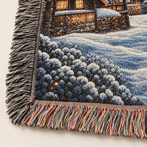 Puede incluir: Una manta de tapiz tejida que muestra una escena invernal con una casa y &aacute;rboles cubiertos de nieve. El dise&ntilde;o utiliza tonos azules, blancos y marrones, con un borde de flecos decorativos en hilos negros, blancos y multicolores.