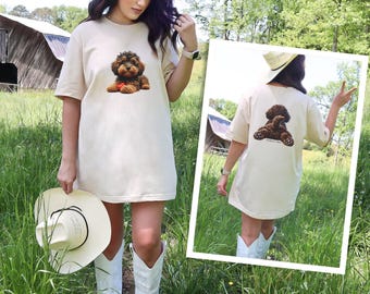 Könnte beinhalten: Ein beiges Kurzarm-T-Shirt mit einer Grafik eines braunen, lockigen Hundes auf der Brust und einer Abbildung desselben Hundes von hinten auf der Rückseite. Das Shirt hat einen Rundhalsausschnitt und eine lockere Passform mit Hunde-Motiv.