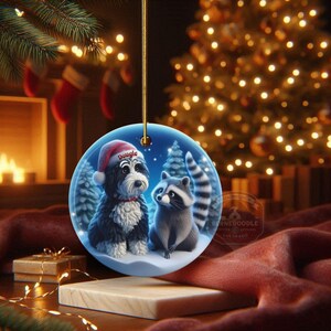 A 3-inch double-sided ceramic Christmas ornament featuring an adorable claymation-style Bernedoodle wearing a red Santa hat personalized  sitting beside a cute raccoon under a snowy winter night sky. The ornament has crisp detailing, soft blue tones, and a warm Christmas glow in the blurred background. Perfect for Bernedoodle lovers, handmade Christmas gift shoppers. High-quality ceramic with vibrant colors, ideal for tree decorating, pet memorial ornaments, or festive seasonal displays.