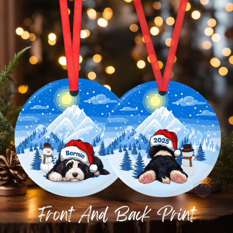 May include: Round Christmas ornament with a winter scene featuring a black and white dog wearing a Santa hat. The ornament has a red ribbon for hanging. The text "Bernie" and "2025" are on the hats. The words "Front And Back Print" are at the bottom.