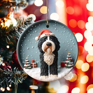 May include: A round Christmas ornament featuring a Bernedoodle dog wearing a Santa hat with the name "Willy". The ornament has a snowy scene with Christmas trees and gifts. The dog is black, white, and brown.