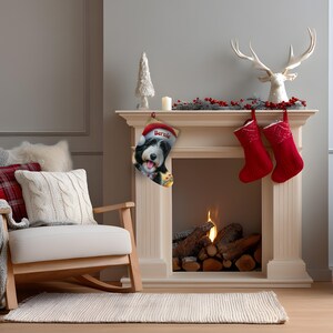 Op de afbeelding: Een versierde open haard met een kerstsok met een hond genaamd "Bernie". Twee rode kerstsokken hangen ernaast. Een witte rendierkop en een kleine witte kerstboom sieren de schoorsteenmantel.