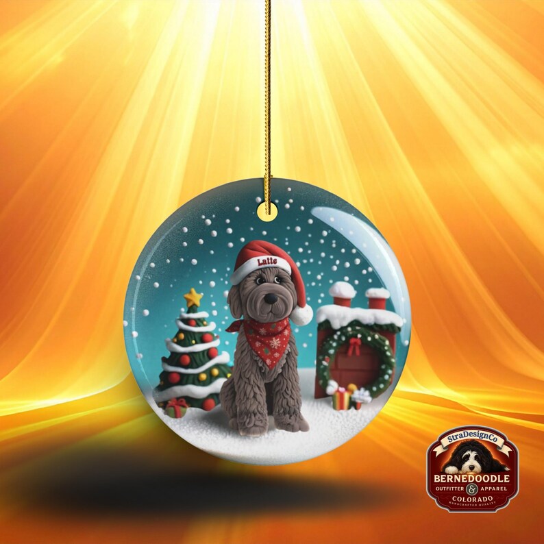 May include: Round Christmas ornament featuring a brown dog wearing a Santa hat and bandana, with the name "Latte" on the hat. The ornament has a Christmas tree, a chimney, and a snowy background. A gold string is attached for hanging.