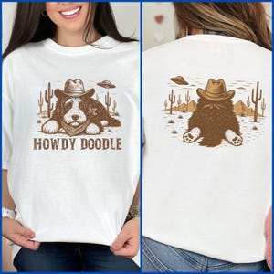 Może przedstawiać: Biała koszulka z grafiką brązowego psa w kapeluszu kowbojskim i bandanie, z napisem "HOWDY DOODLE". Projekt zawiera kaktusy i UFO. Tył koszulki przedstawia ten sam wz&oacute;r psa.
