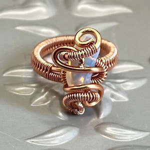 May include: A ring featuring a white opal stone encased in rose gold wire. The wire is twisted and forms a spiral around the stone.