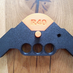 Op de afbeelding: Zwart plastic gereedschap met een oranje handvat en een knop. Het gereedschap heeft vier gaten en de tekst "R40" op het oranje handvat.