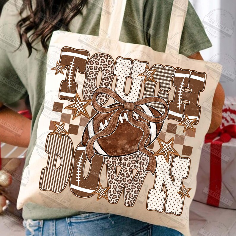 Peut inclure: Un sac fourre-tout couleur cr&egrave;me avec le texte TOUCH DOWN en grandes lettres majuscules. Les lettres sont d&eacute;cor&eacute;es de motifs l&eacute;opard, &eacute;cossais et &agrave; pois. Un ballon de football marron avec un grand n&oelig;ud marron est au centre avec des &eacute;toiles.