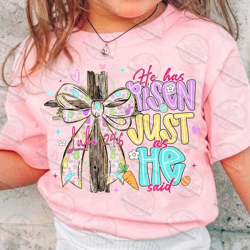May include: Pink t-shirt with a colorful Easter-themed graphic. The design features a wooden cross adorned with a patterned bow, the text "He has Risen JUST as HE said", and the Bible verse Luke 24:6.