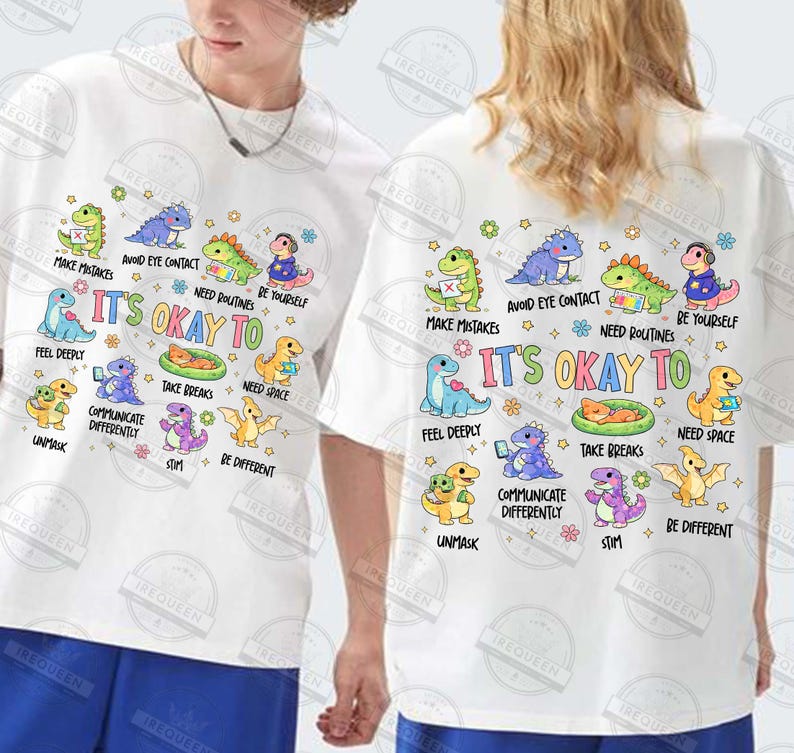 May include: White t-shirts with a colourful graphic design featuring cartoon dinosaurs and the text "It's Okay To." The design includes phrases like "Make Mistakes" and "Be Yourself."