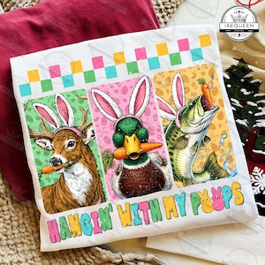 May include: White t-shirt with a colorful graphic featuring a deer, duck, and fish, each wearing bunny ears and holding carrots. The text "HANGIN' WITH MY PEEPS" is below the images. A fun, Easter-themed design.
