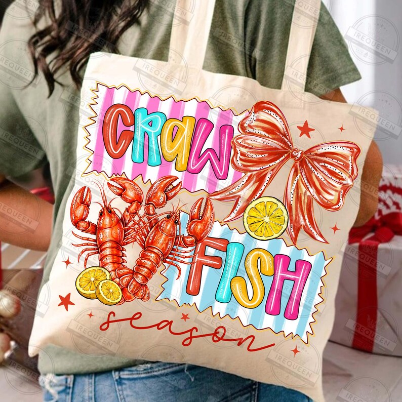 May include: A beige tote bag with a colorful design. The design includes the words "CRAWFISH" in a playful font, along with illustrations of red crawfish, lemon slices, and a red bow. The word "season" is written in a cursive font.