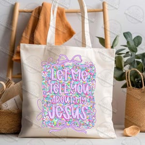 May include: Cream-colored tote bag with the text "Let Me Tell You About My Jesus" in a colorful floral design. The bag has a rectangular design with a bow and daisy accents.