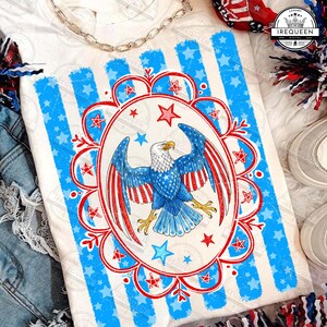 May include: White t-shirt featuring a patriotic design with a bald eagle, stars, and stripes in red, white, and blue. The design is centered within a blue striped border with star accents, perfect for Independence Day celebrations.