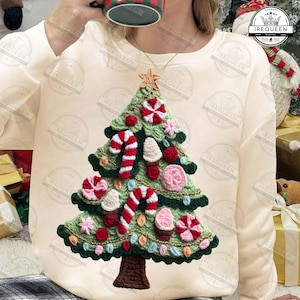 Puede incluir: Sudadera color crema con un diseño detallado de árbol de Navidad tejido a ganchillo. El árbol está adornado con bastones de caramelo rojos y blancos, adornos rosas y rojos y una estrella dorada. El diseño está intrincadamente elaborado con hilo verde y marrón.