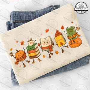 May include: A cream-colored sweatshirt featuring a graphic print of anthropomorphic pumpkins, books, and coffee cups. The characters wear scarves and boots, surrounded by falling autumn leaves. The text "AUTUMN STORIES" is printed on one book.
