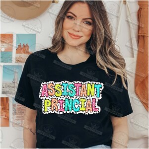May include: A black t-shirt with the words "Assistant Principal" in colorful letters with white polka dots on a black background.