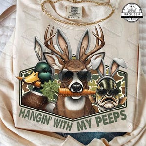 May include: Beige sweatshirt with a graphic featuring a deer, duck, and fish wearing sunglasses and bunny ears, each holding a carrot. The text "HANGIN' WITH MY PEEPS" is below the graphic.