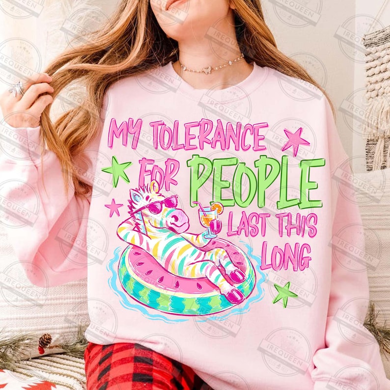 Puede incluir: Sudadera rosa claro con el texto "My Tolerance For People Last This Long". El dise&ntilde;o presenta una cebra con gafas de sol flotando en una boya con forma de sand&iacute;a, sosteniendo un c&oacute;ctel. Tambi&eacute;n incluye estrellas verdes y rosas.