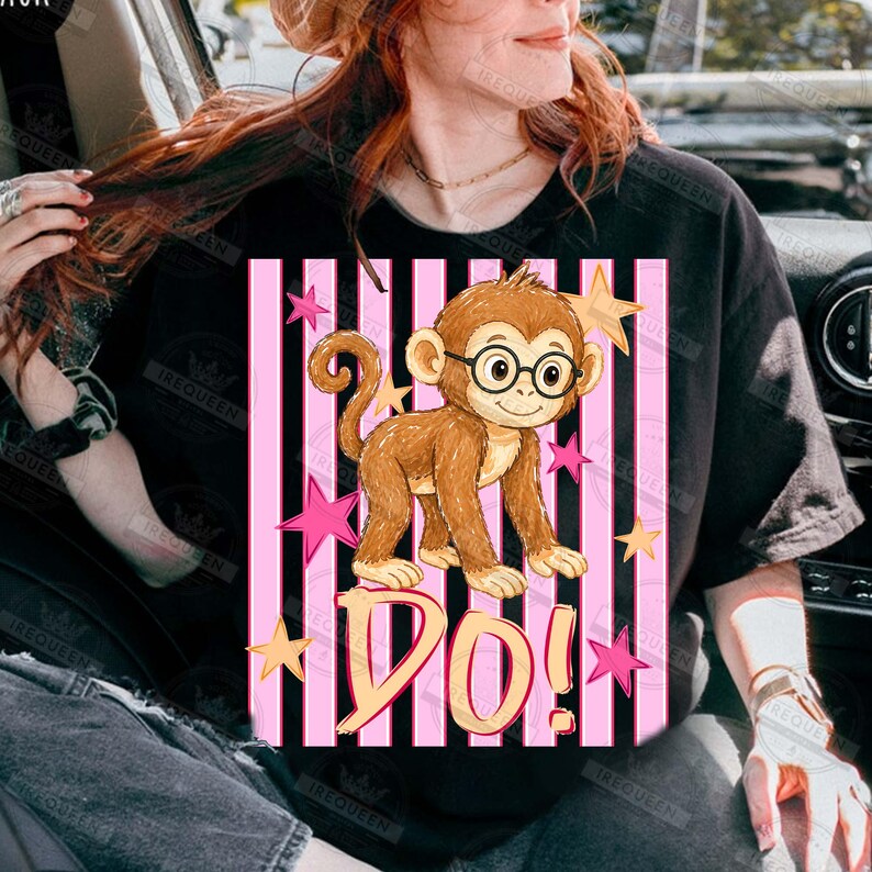 Puede incluir: Camiseta negra con un mono de dibujos animados con gafas, sobre un fondo de rayas rosas y negras. La palabra "DO!" est&aacute; escrita debajo del mono, con estrellas rosas y amarillas dispersas.