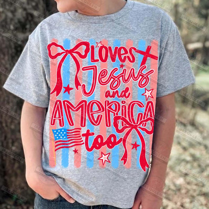 Puede incluir: Una camiseta gris con la frase "Loves Jesus and America too" en rojo. El dise&ntilde;o incluye lazos rojos, estrellas y una peque&ntilde;a bandera estadounidense. El fondo tiene rayas verticales rojas y azules.