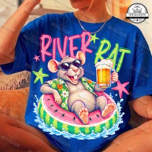 May include: A blue t-shirt featuring a graphic of a rat wearing sunglasses and a floral shirt, floating in a watermelon-patterned inner tube while holding a glass of beer. The text RIVER RAT is printed in pink and green above the illustration.