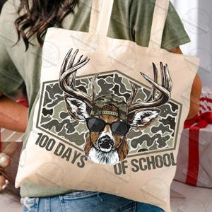Puede incluir: Bolso tote beige con un ciervo con gafas de sol y gorra de camuflaje. El ciervo est&aacute; dentro de un hex&aacute;gono de camuflaje con el texto "100 Days of School". El bolso es de color beige claro.