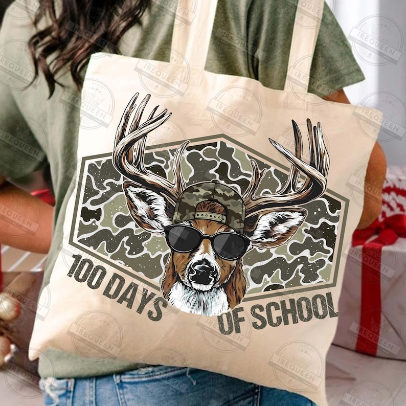 Puede incluir: Bolso tote beige con un ciervo con gafas de sol y gorra de camuflaje. El ciervo est&aacute; dentro de un hex&aacute;gono de camuflaje con el texto "100 Days of School". El bolso es de color beige claro.
