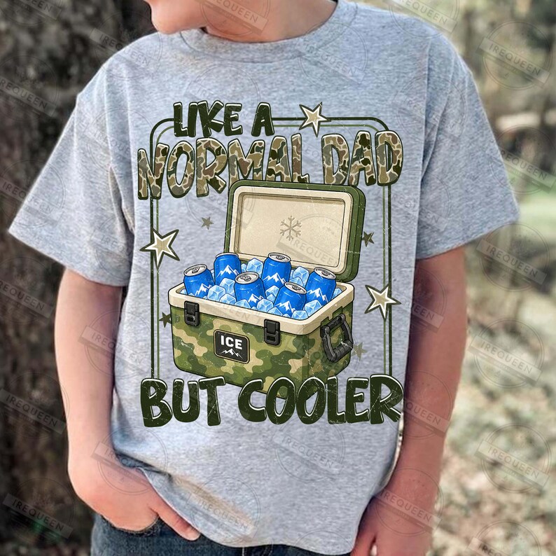 May include: A gray t-shirt with the text "LIKE A NORMAL DAD BUT COOLER" in a camouflage design. The graphic includes a cooler filled with ice and blue cans. The shirt is a casual wear item.