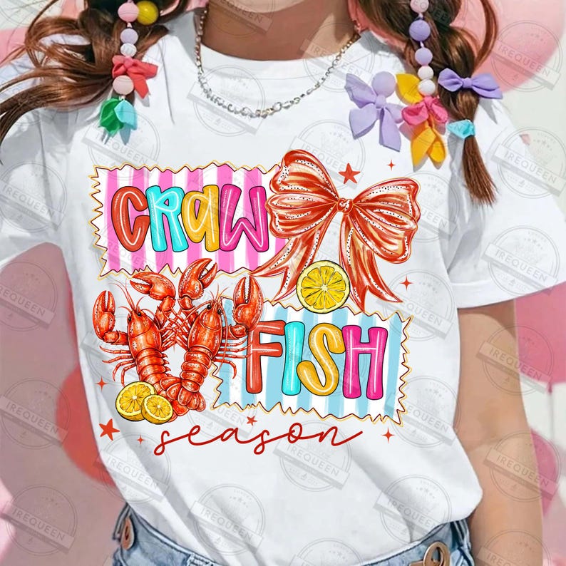 May include: White t-shirt with a colorful graphic design. The design features the words "CRAW FISH" in bubble letters, along with illustrations of crawfish, a bow, and lemon slices. The word "season" is written in cursive.