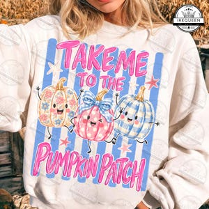 May include: A cream-colored sweatshirt featuring a graphic of three cartoon pumpkins with arms and legs. The text reads "TAKE ME TO THE PUMPKIN PATCH" in pink. The pumpkins have floral, polka dot, and blue gingham patterns with small stars.