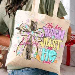 May include: A beige tote bag featuring a wooden cross with a pastel bow and the text "He has risen, just as He said." The design includes Easter-themed elements like bunnies, carrots, and eggs. The scripture Luke 24:6 is also visible.