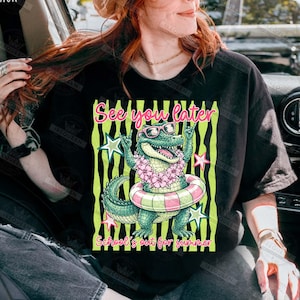 May include: Black t-shirt featuring a cartoon alligator wearing sunglasses and a floral lei, inside a pink and white striped inner tube. The text "See you later" and "School's out for summer" are also displayed.