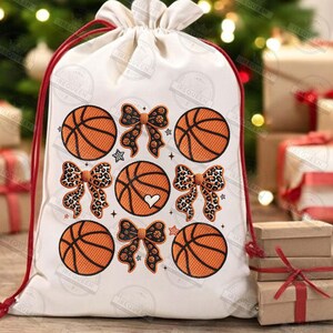 May include: A white drawstring gift bag featuring orange basketballs and decorative bows. The bows have a leopard print design. The bag has a red drawstring closure and is decorated with small stars and a heart.