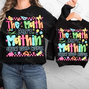 Puede incluir: Sudaderas negras con el texto "The Math Ain't Mathin' Show Your Work" en letras coloridas y gr&aacute;ficos. El dise&ntilde;o incluye mariposas, tijeras y un l&aacute;piz. Una sudadera es para adultos, la otra para ni&ntilde;os.