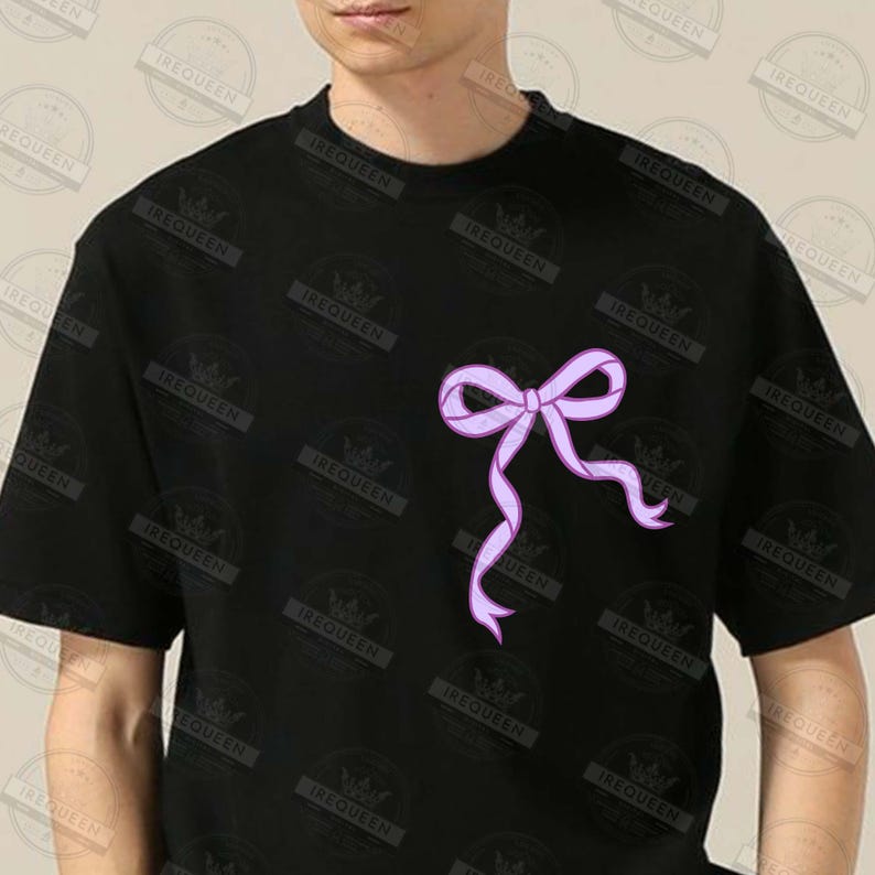 May include: Black t-shirt featuring a light purple bow design on the front. The bow has flowing ribbons and is centered on the chest. The shirt is short-sleeved and made of a soft material.